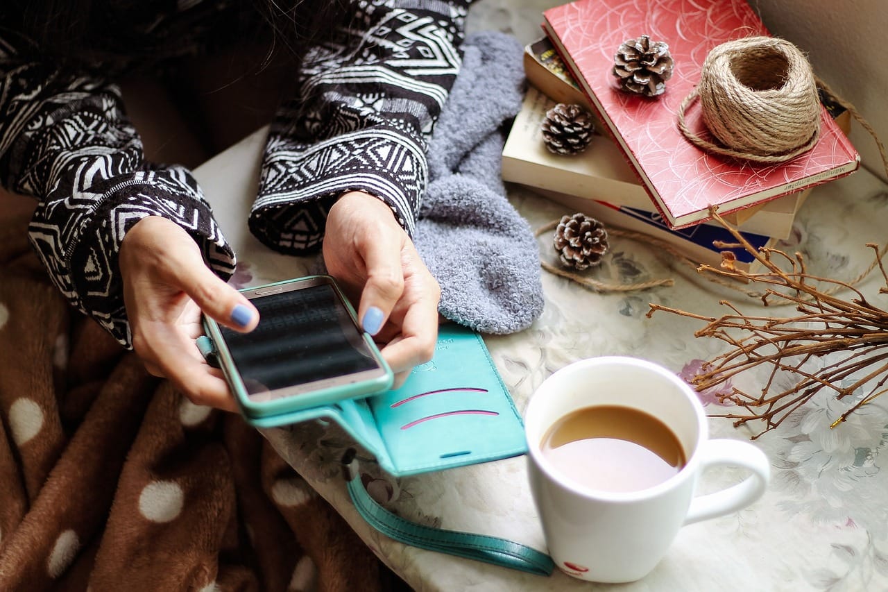 Girl with blue nails holding her phone planning her work during winter with a cup of tea.